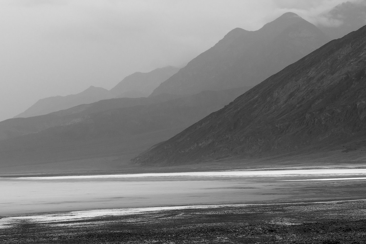 Black and white landscape of a misty mountain range reflected in a calm desert salt flat lake.