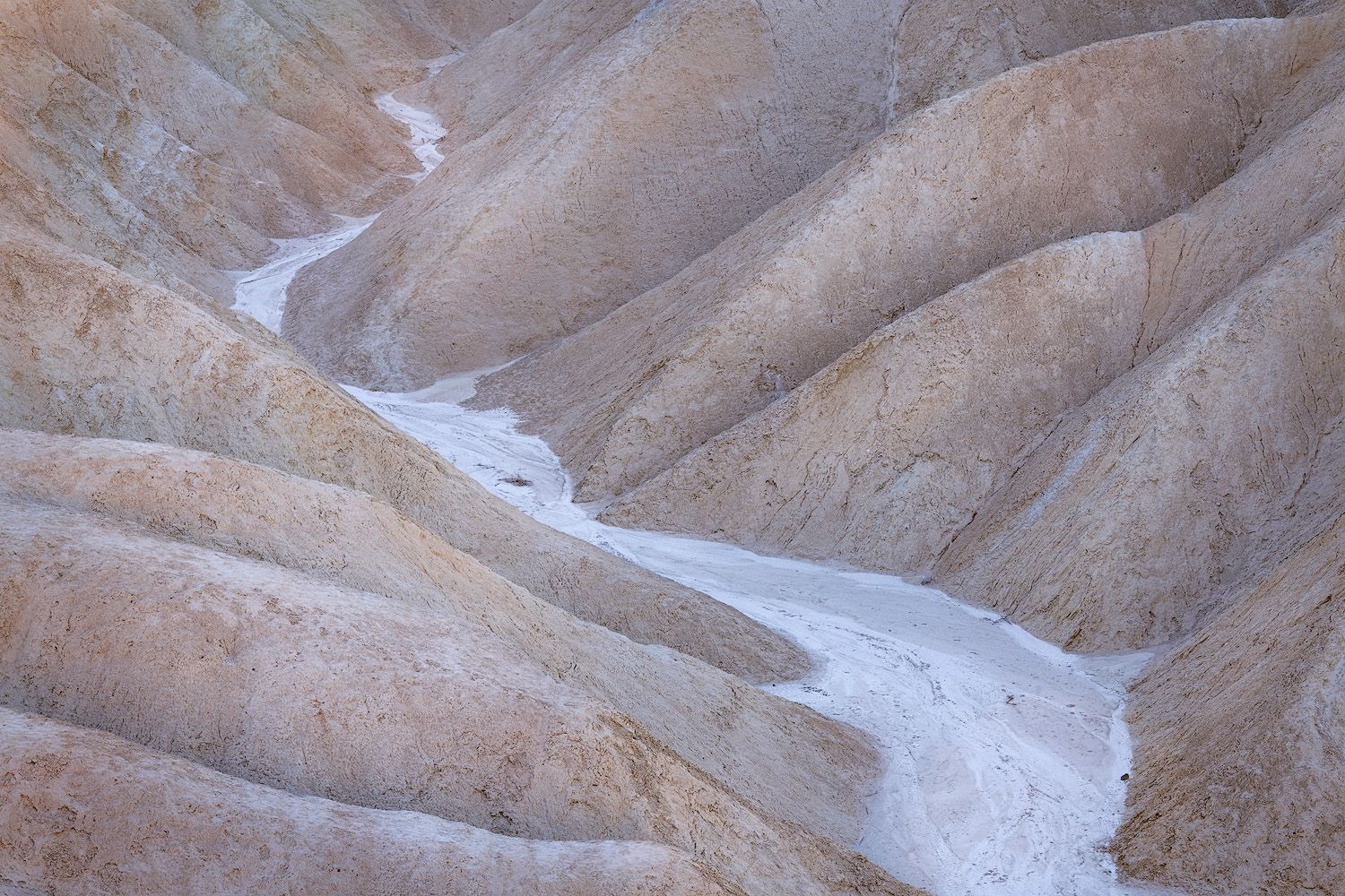 Rugged desert mountain landscape with layered rock formations in warm earth tones under a bright sky.