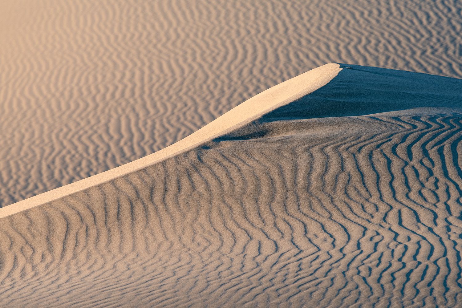 Aerial view of undulating sand dunes creating mesmerizing ripple patterns in a desert landscape at sunset.
