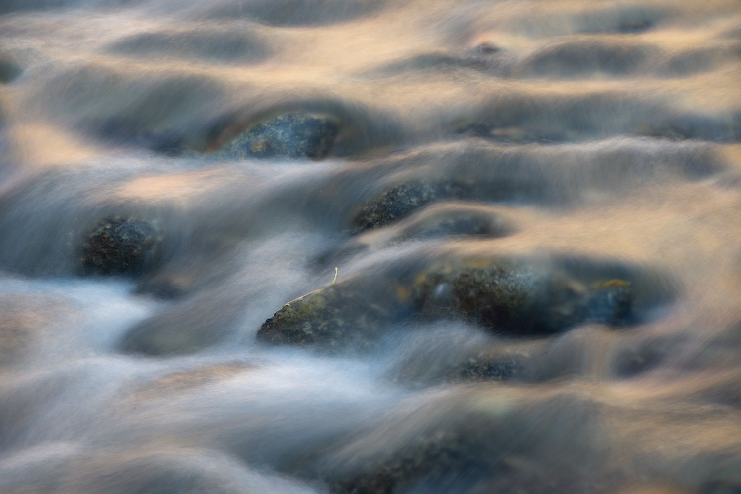 Long exposure photograph captures smooth flowing water creating ethereal misty patterns against a dark background.