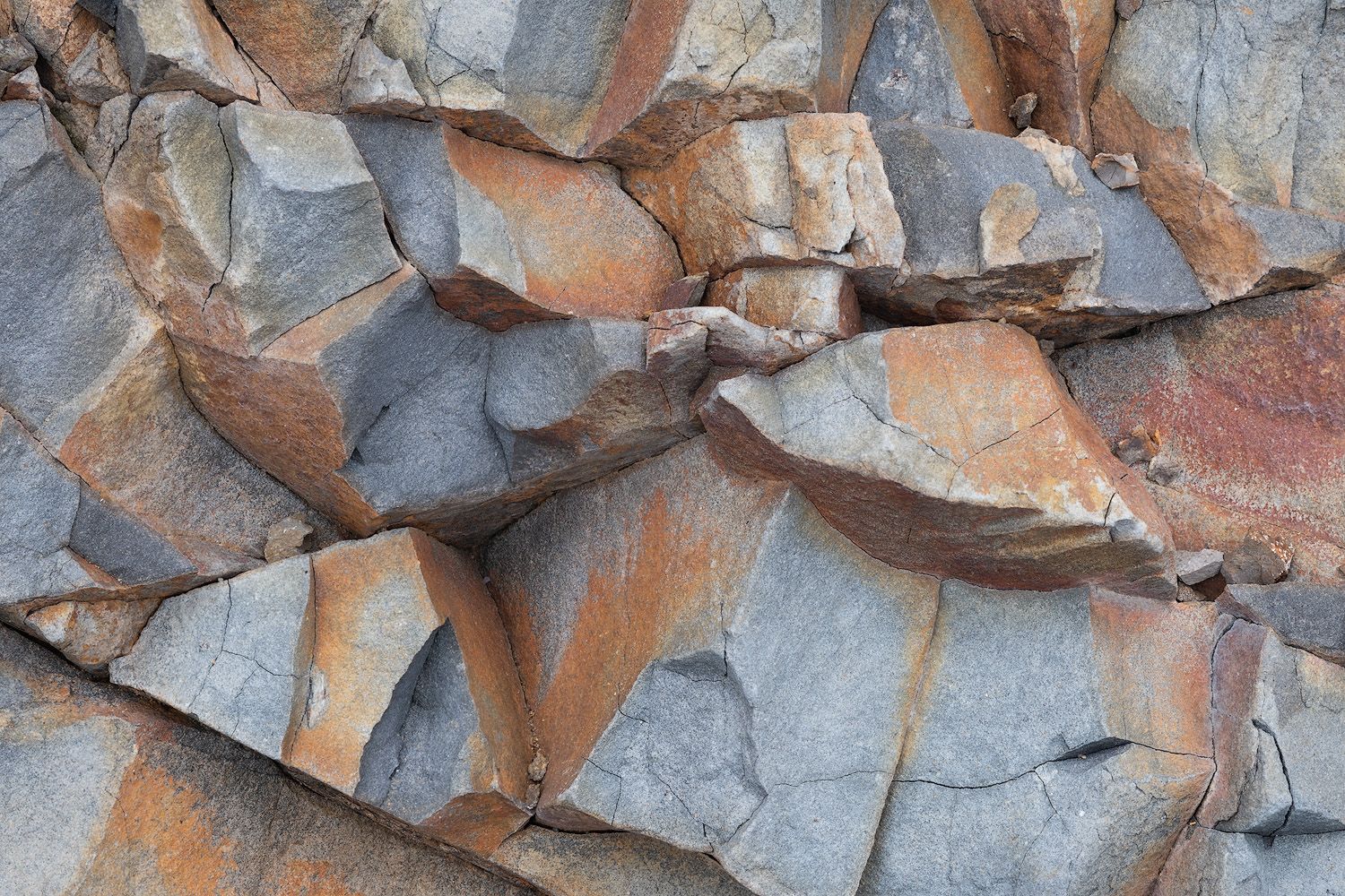Fractured rock face displaying angular patterns in orange and gray tones.