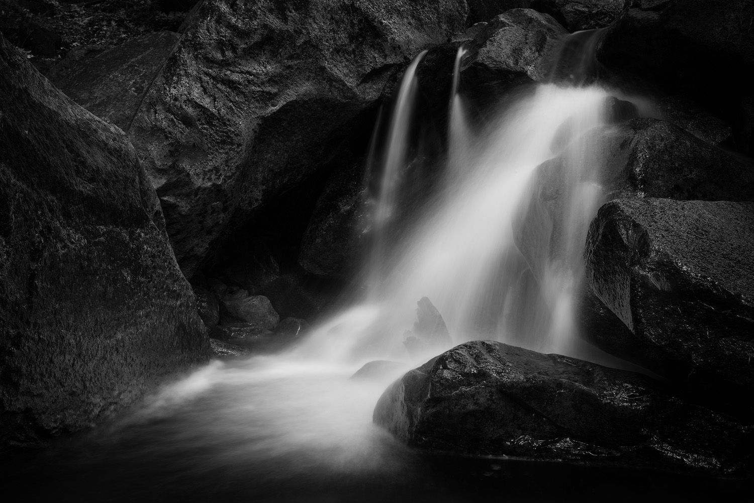 Dramatic black and white waterfall cascading over dark rocky cliffs with smooth flowing water captured using long exposure.