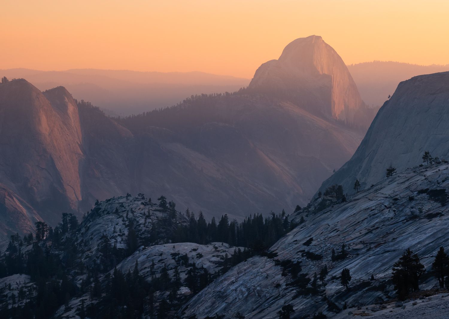 Half Dome glows at sunset with dramatic mountain silhouettes in Yosemite National Park.