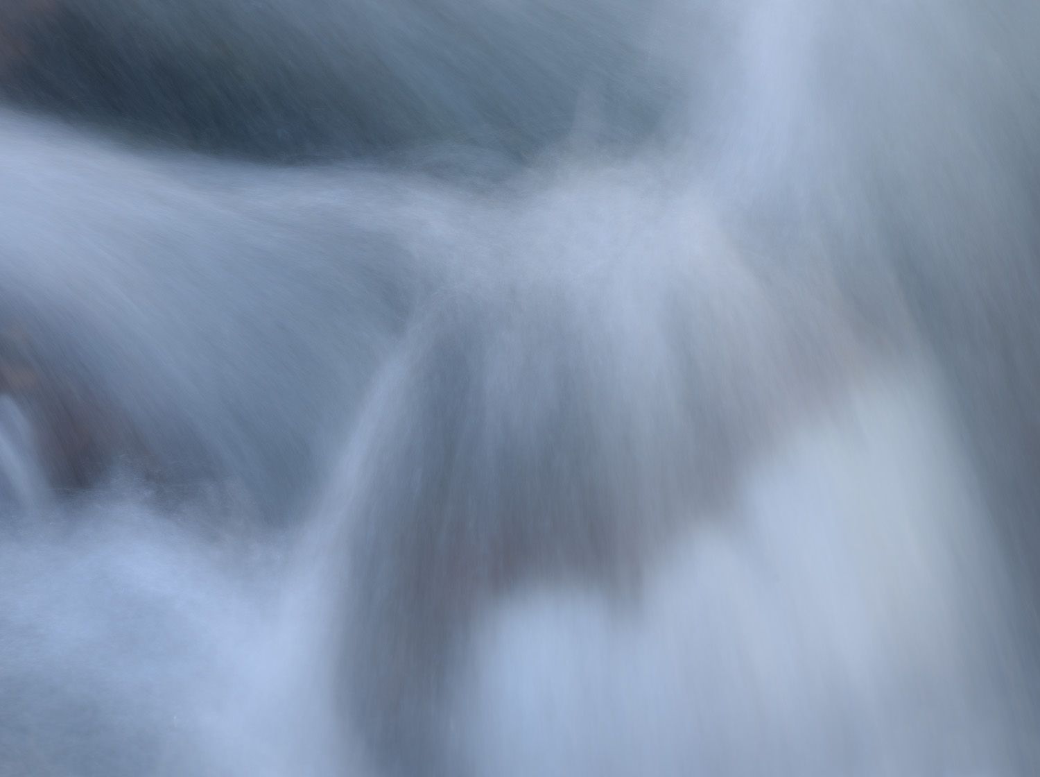 Long exposure photograph of flowing water creates a soft, ethereal effect with misty white and blue tones.