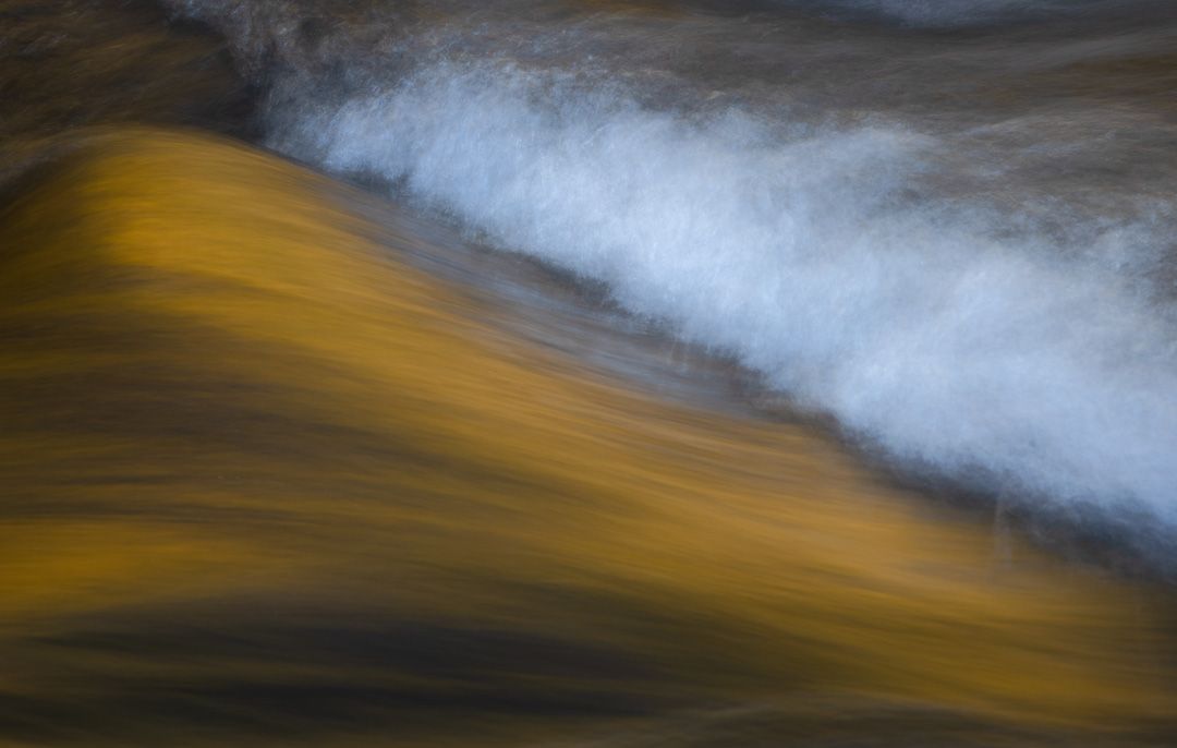 Abstract long exposure of flowing water creating golden and white streaks against dark background.