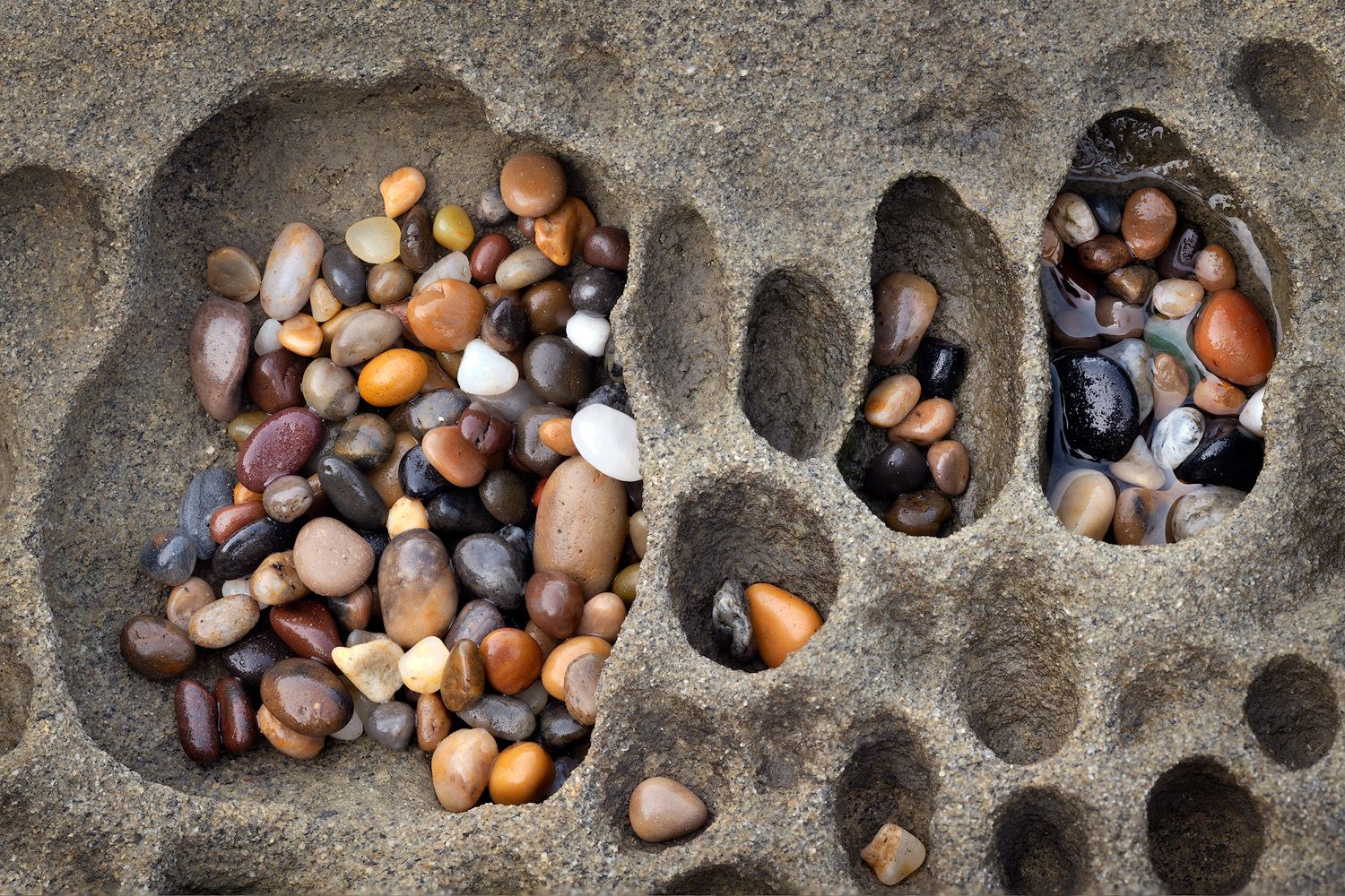Colorful beach pebbles and stones collected in natural holes formed in sandstone tafoni.