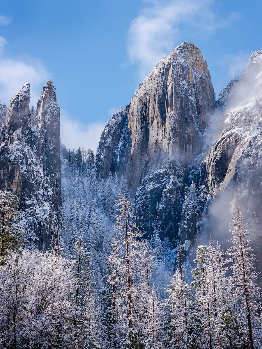 Snow-covered granite peaks of Yosemite Valley rise dramatically against a bright blue winter sky.
