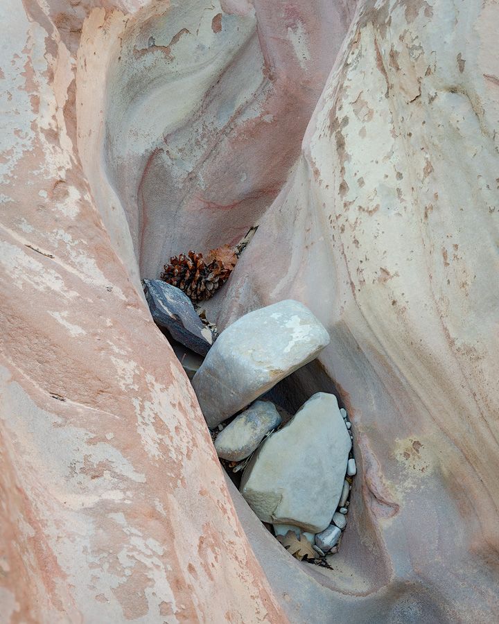 Close-up of smooth pink sandstone rock formation with small stones nestled in a narrow crevice.