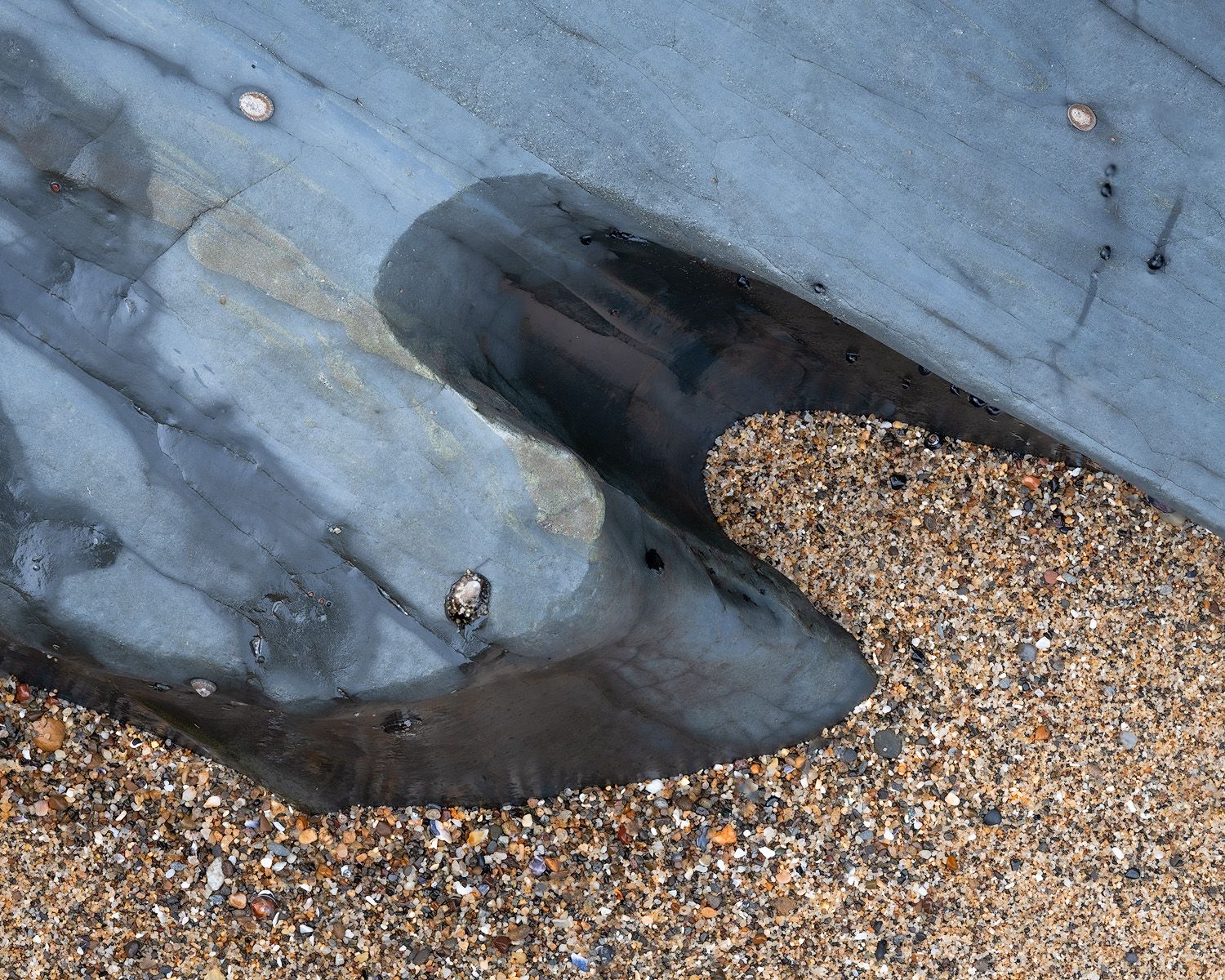 Dark rock formation with sand creates abstract patterns on a beach.