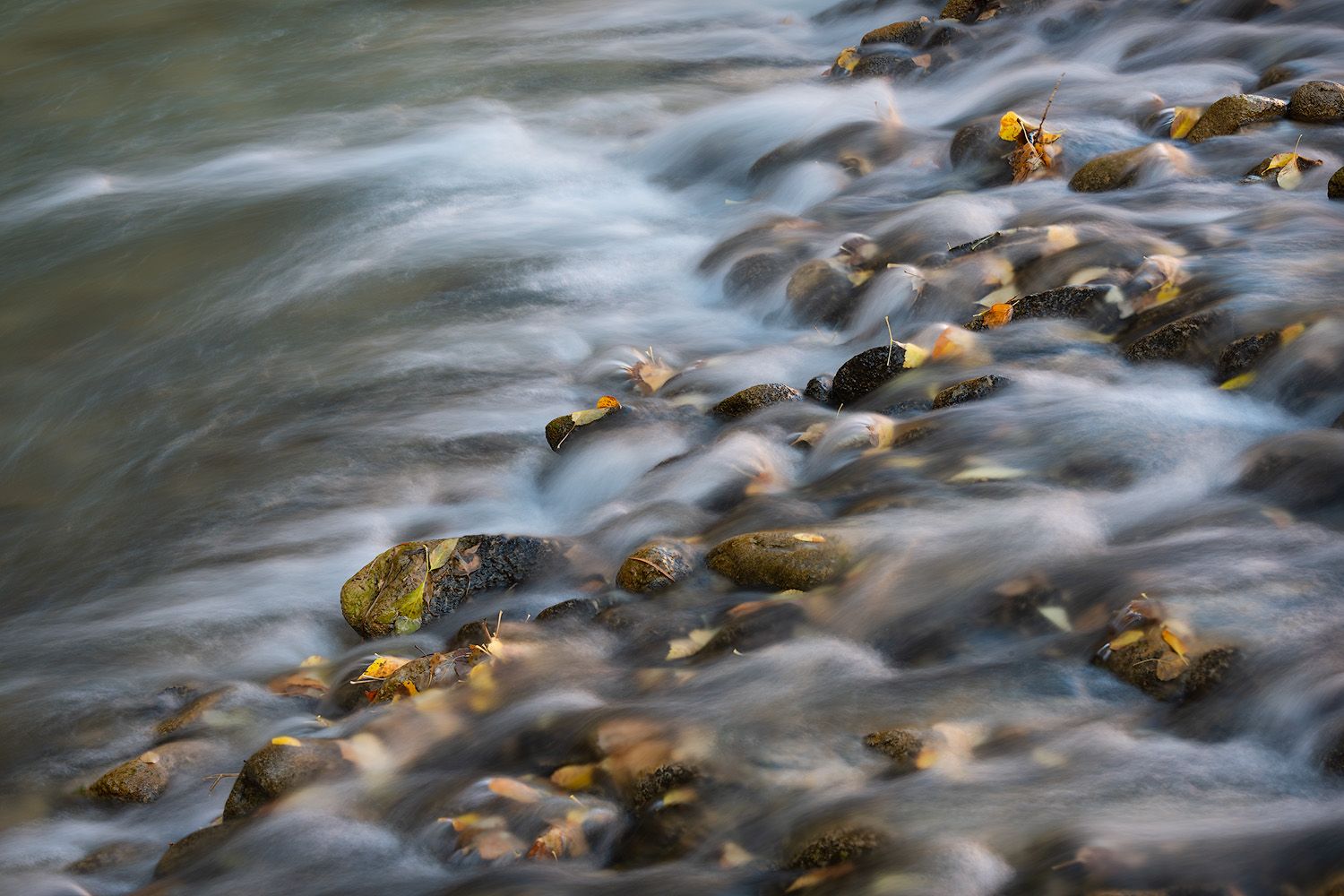 Long exposure photograph of flowing water over smooth river rocks creating a silky motion effect in nature.
