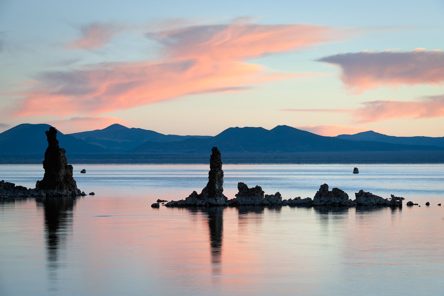 Silhouettes of tufa formations against pastel sunrise sky over Mono Lake.