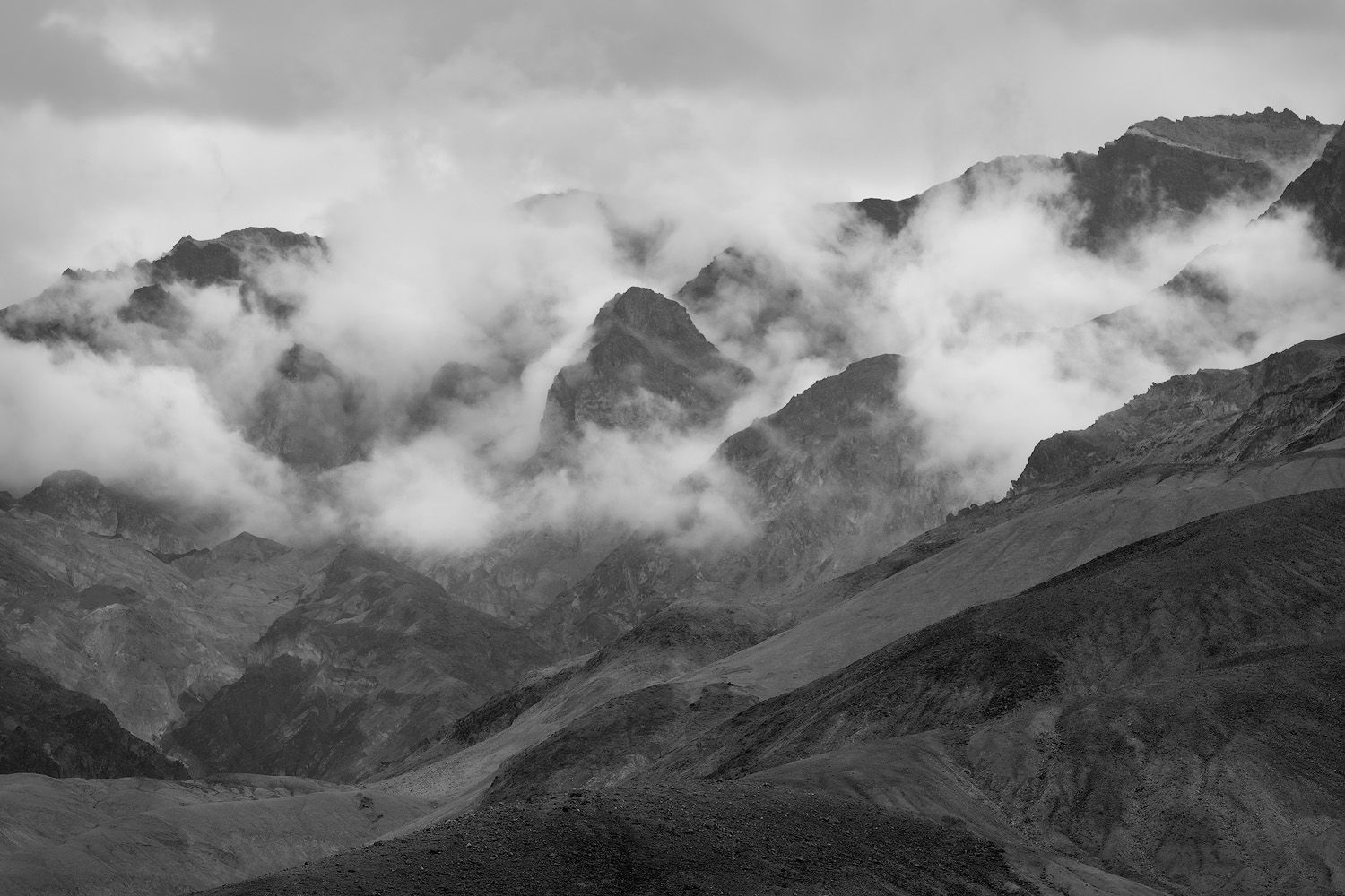 Dramatic mountain peaks emerge through swirling clouds in black and white.