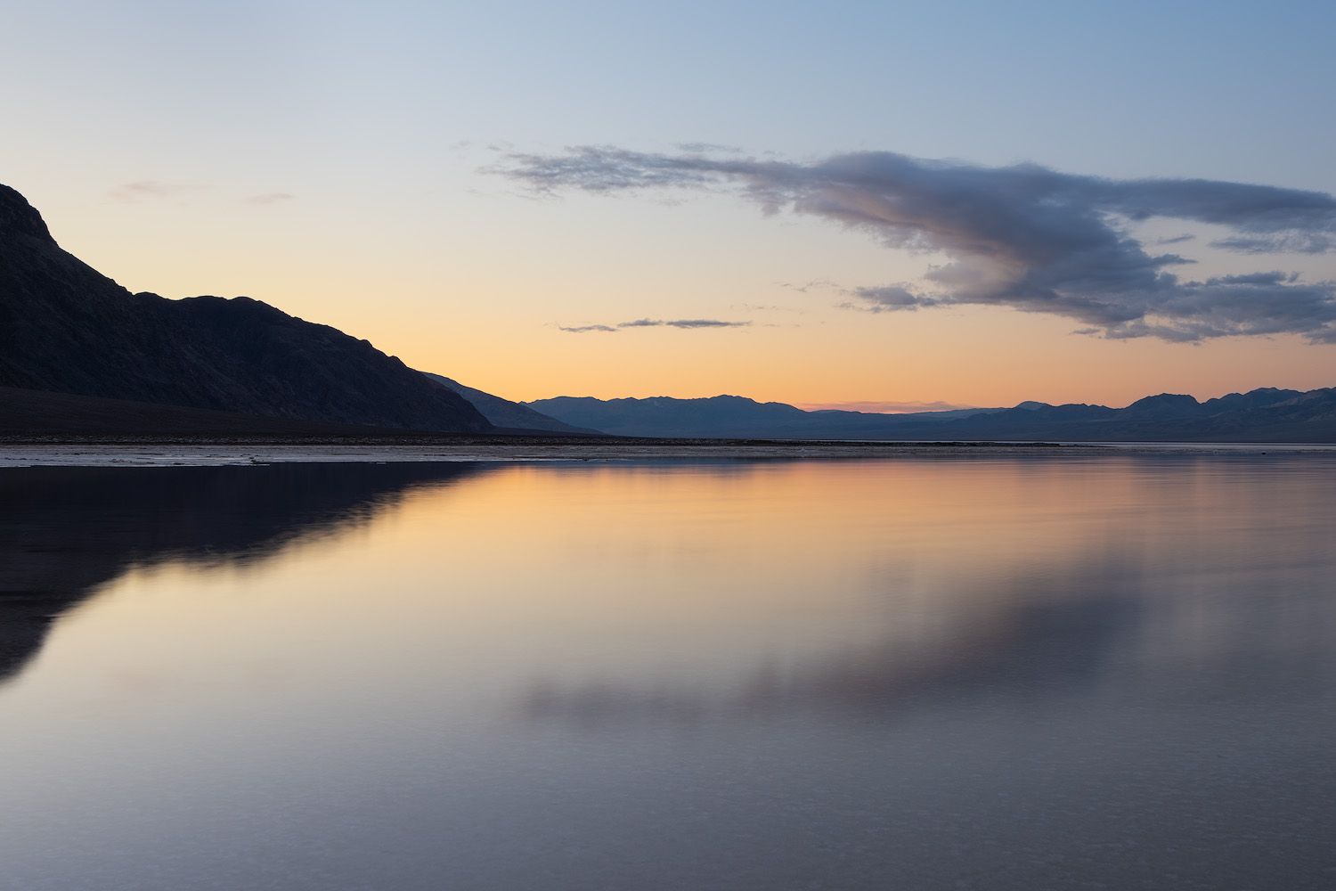 Serene lake at sunset with mountains silhouetted against the colorful sky.