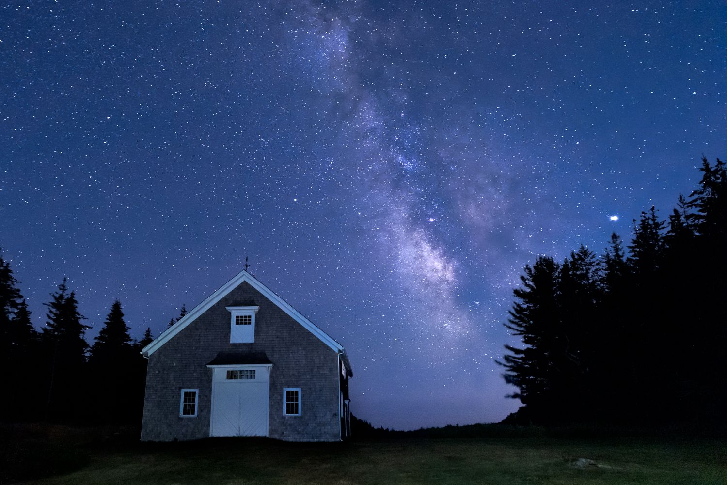Rustic barn under a starry night sky with the Milky Way visible overhead.