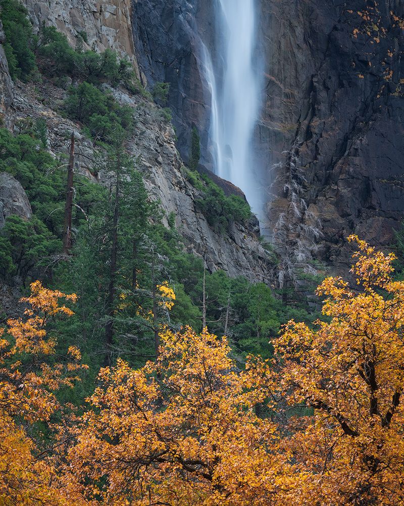 Majestic waterfall cascades down rocky cliffs with golden autumn trees in the foreground.
