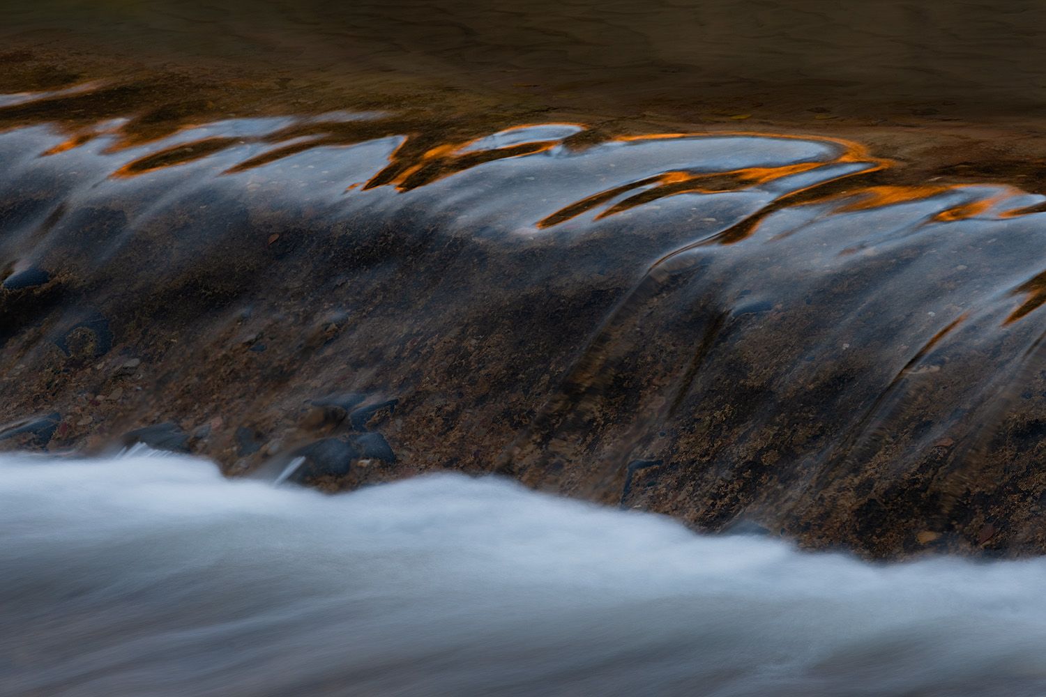 Long exposure photograph shows silky smooth water cascading over rocks in a mountain stream.