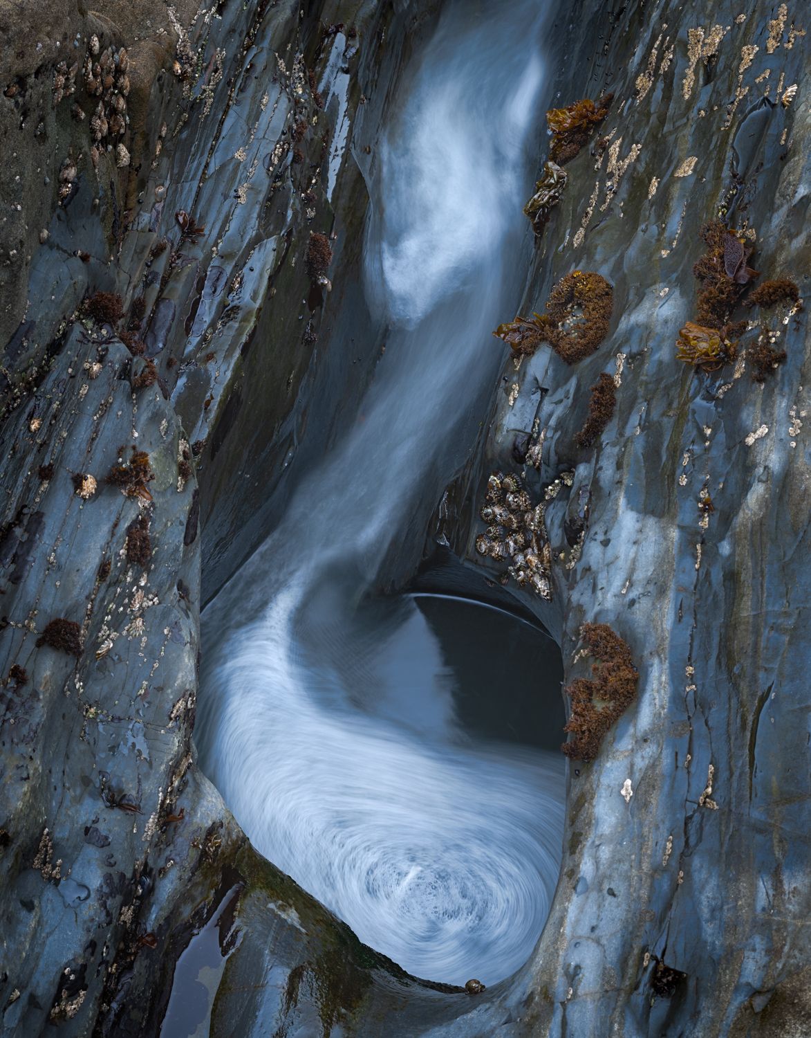 Long exposure water draining through blue-tinted rock creating smooth flowing patterns.