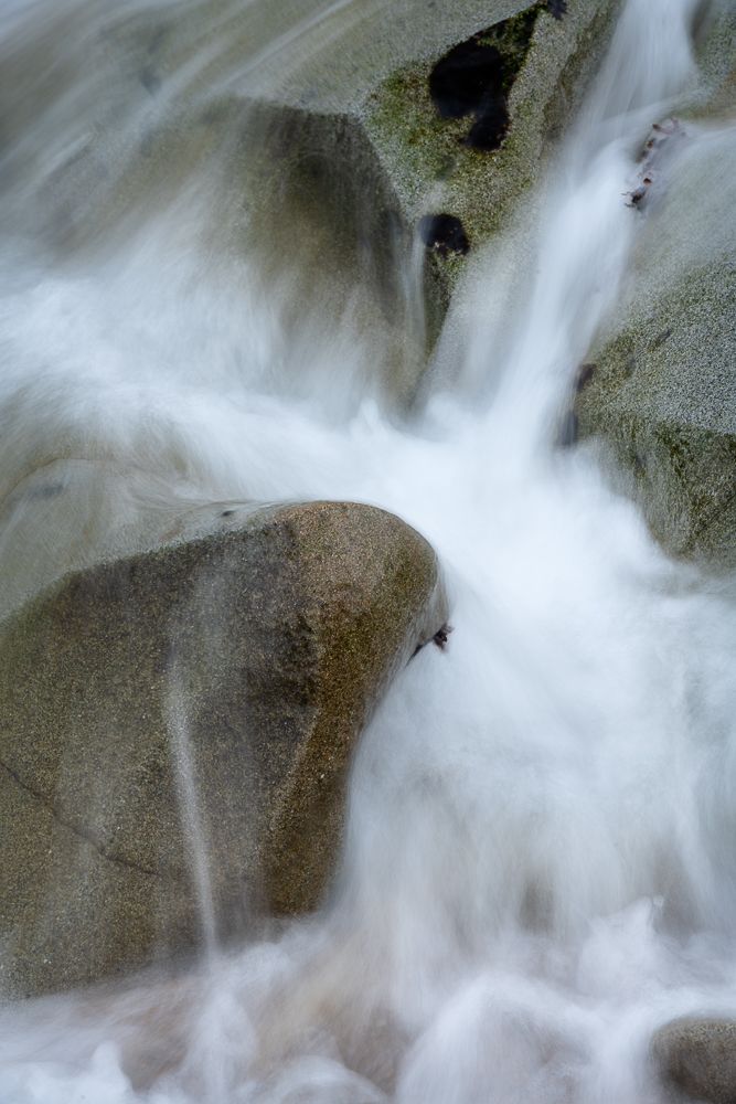 White water cascading over smooth granite rocks creates a dreamy long exposure waterfall effect.