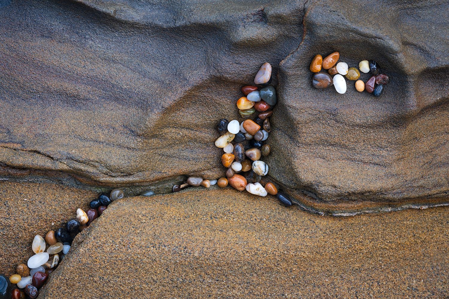 Collection of smooth colorful pebbles and rocks arranged along a rocky beach.