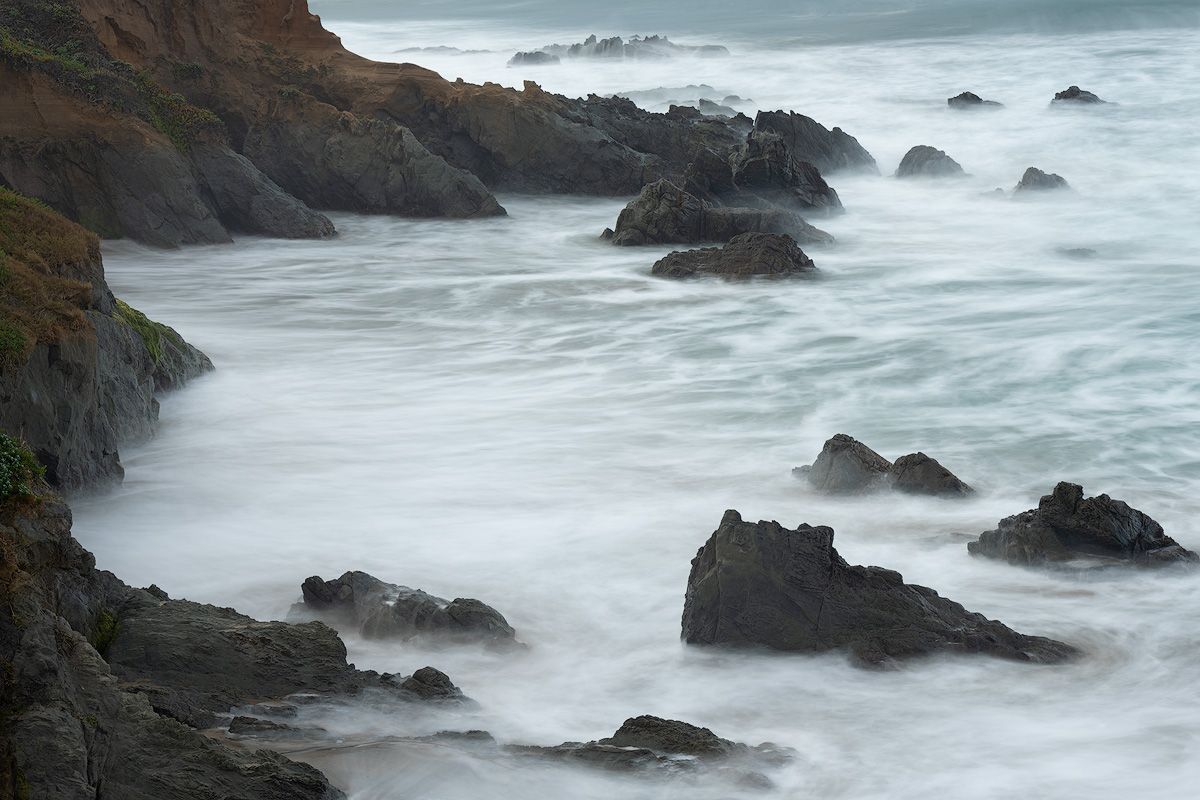 Rocky coastal shoreline with misty waves crashing against dark cliffs.