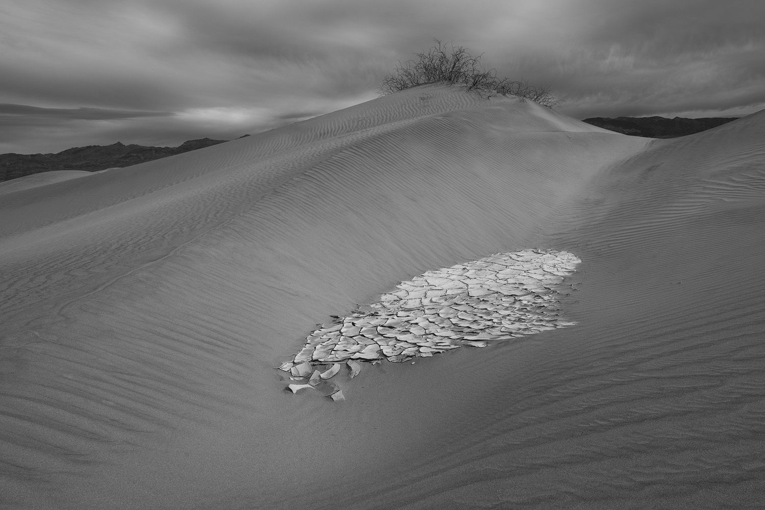 A dramatic black and white image of desert sand dunes with a patch of textured white sand.