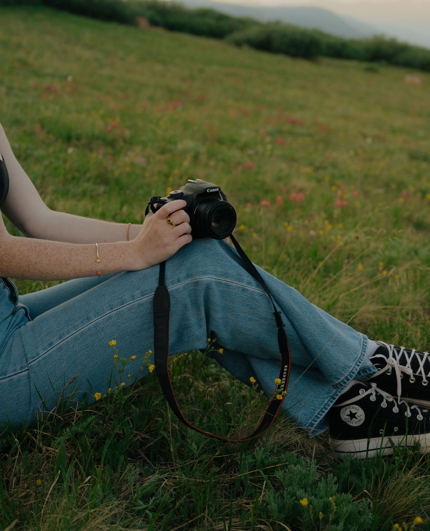 Blue Converse sneakers lying in grass with wildflowers at sunset.