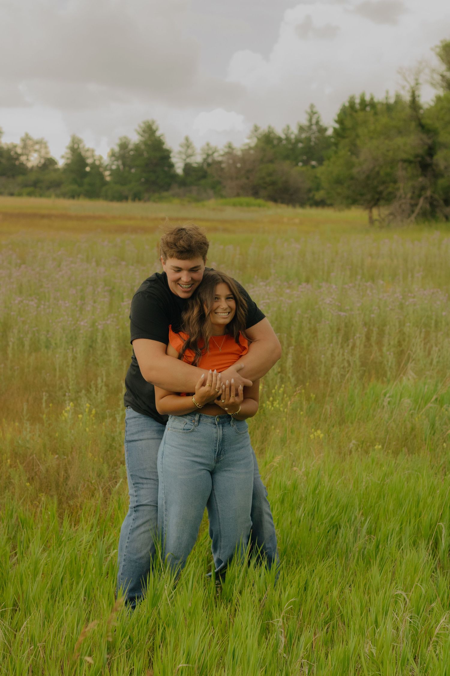 A couple embraces while standing in a tall grass field on a cloudy day.