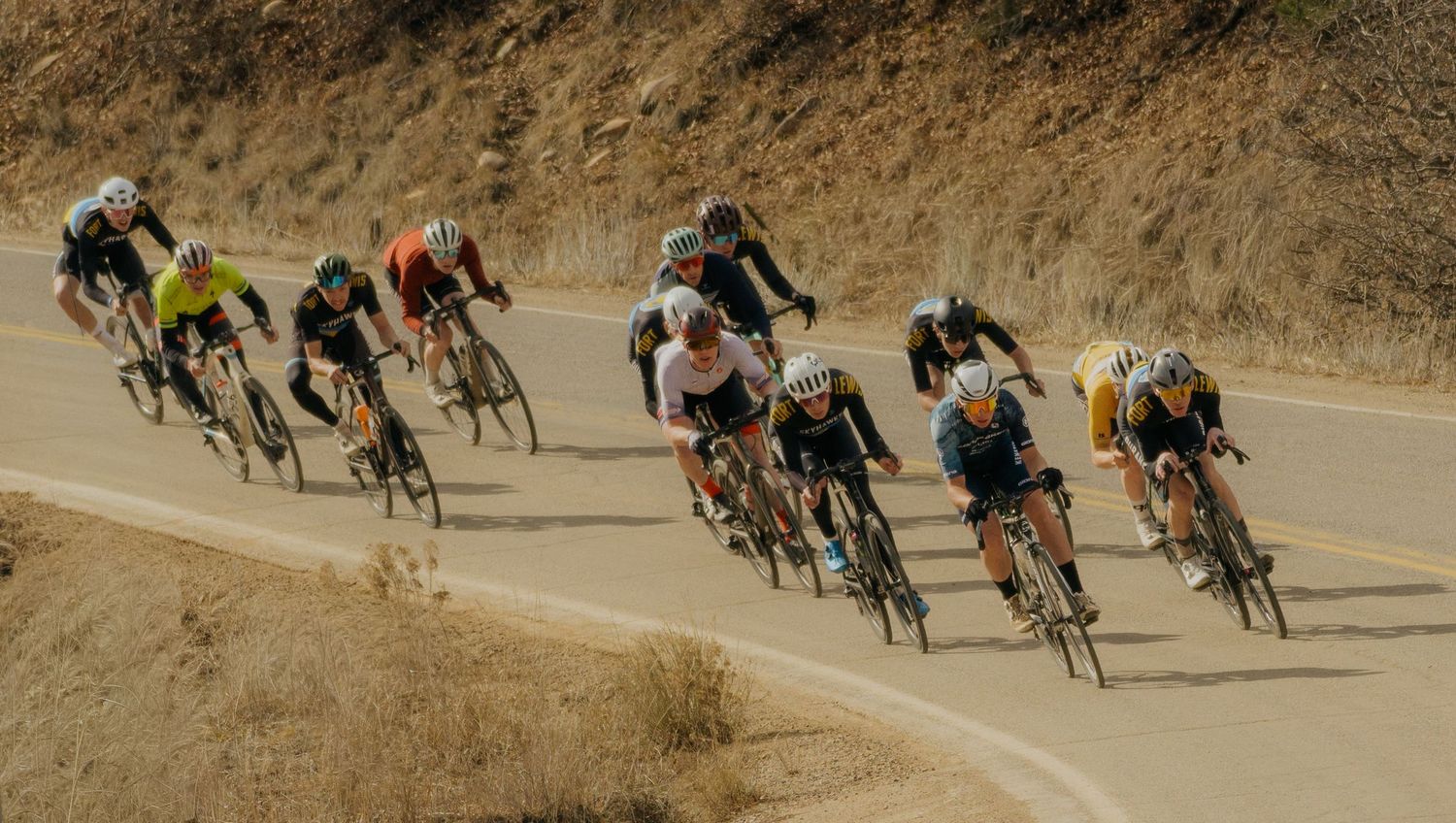 A group of cyclists racing along a winding mountain road during a competitive cycling event.