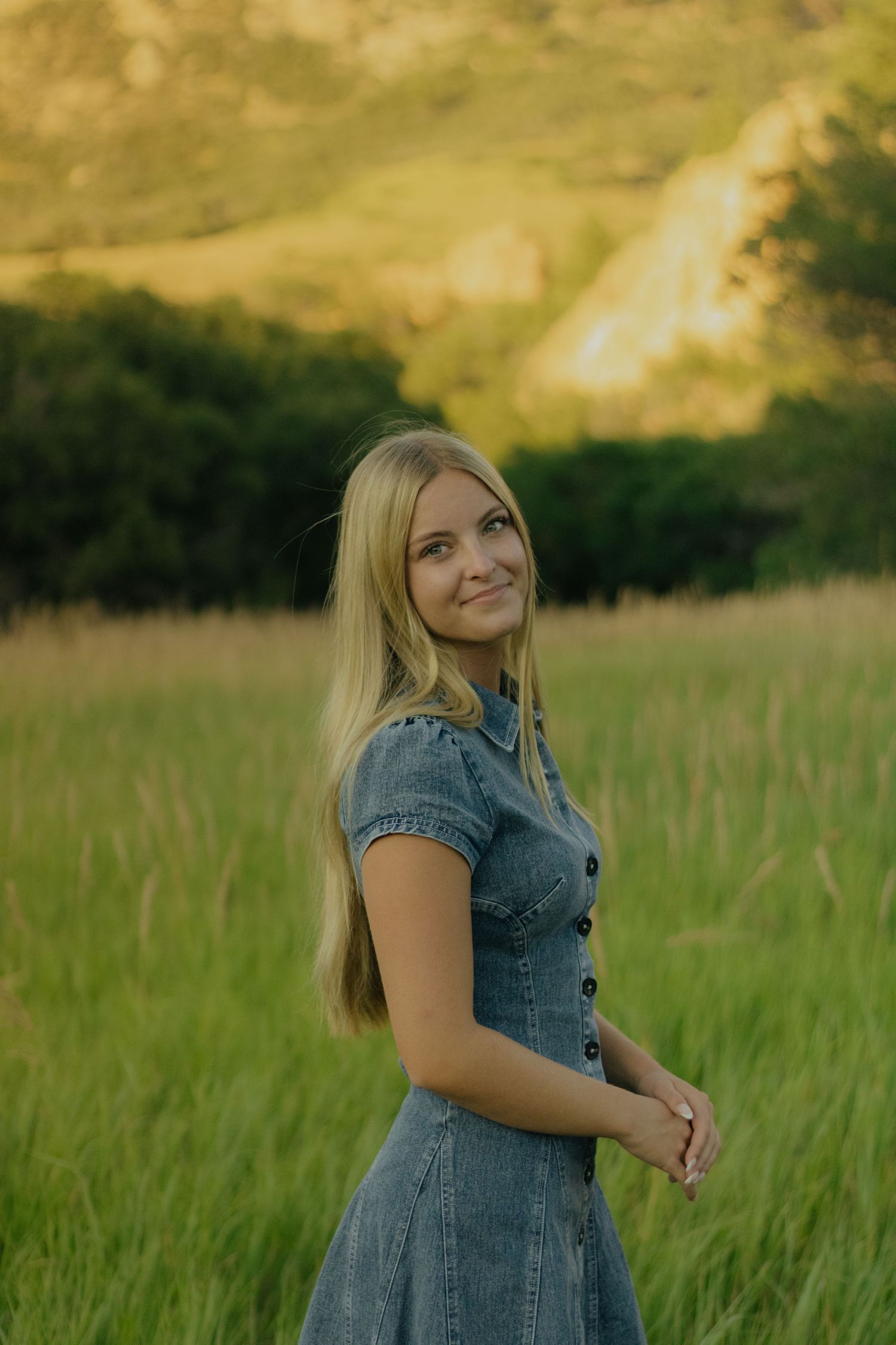 A person in a denim dress spins joyfully in a sunlit meadow during golden hour.