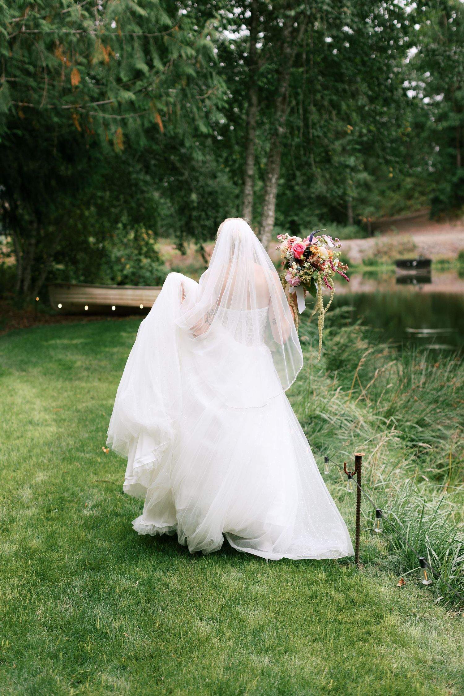 Flowing white wedding dress cascades across green grass in an outdoor garden setting - Adrianna Elizabeth Photography.