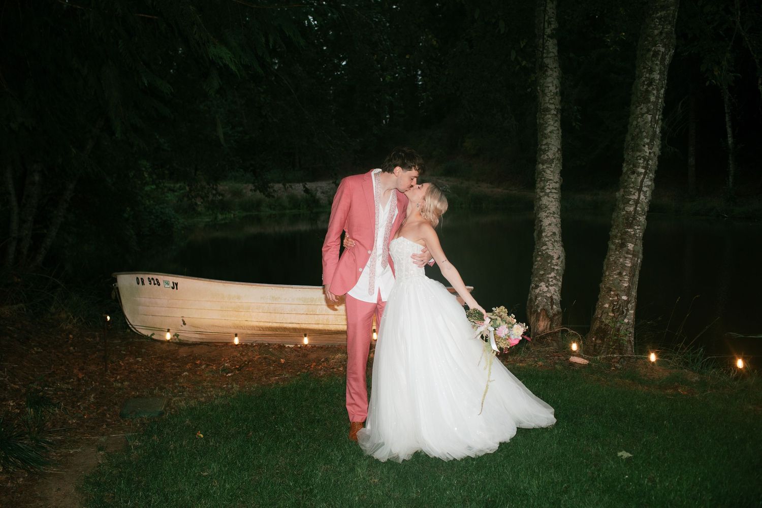Evening wedding couple kiss during reception scene with string lights glowing in dark forest setting-Adrianna Elizabeth Photography.