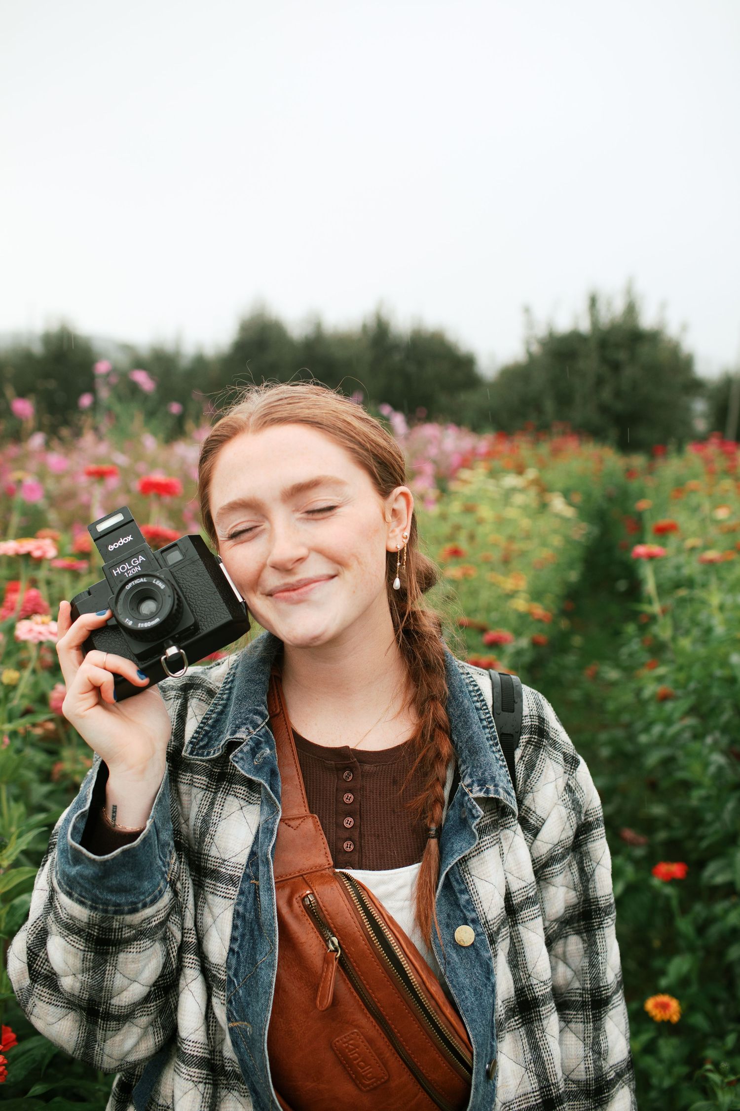 Adrianna Elizabeth photography branding session poses playfully with a vintage camera in a blooming flower garden.