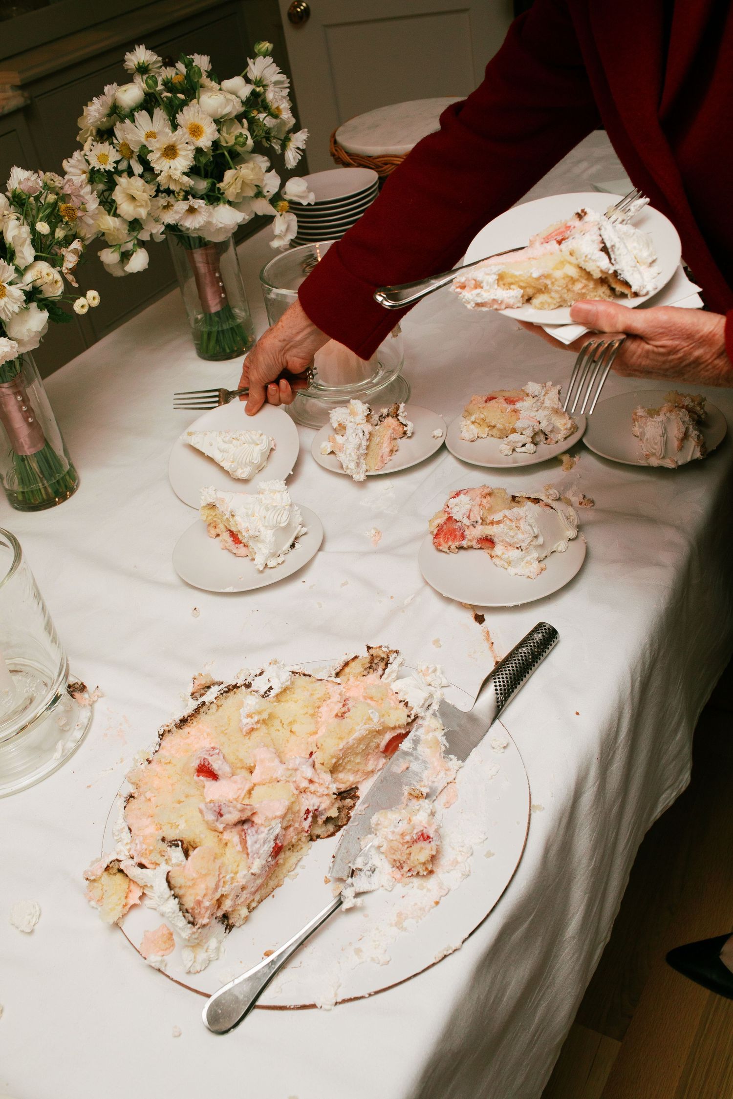 Messy dessert plates with leftover cake crumbs on white tablecloth next to vase of white flowers.