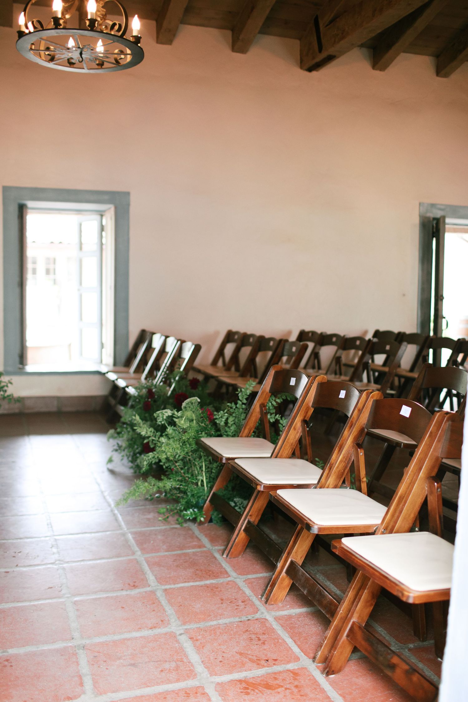 Empty restaurant dining room with wooden chairs, terracotta tile floors, and rustic ceiling beams and chandelier.