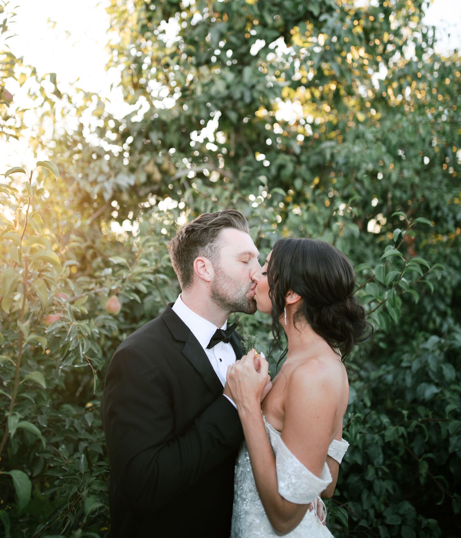 A romantic couple shares intimate kisses in a garden setting during golden hour with lush greenery in the background.