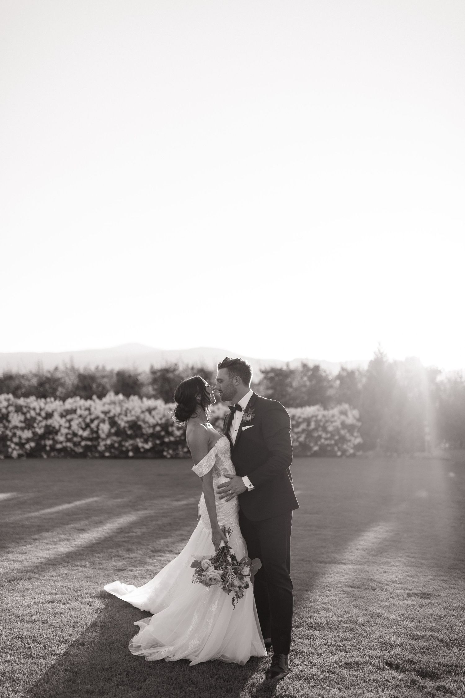 A romantic black and white photo series of newlyweds embracing in a sunlit garden with blooming flowers.