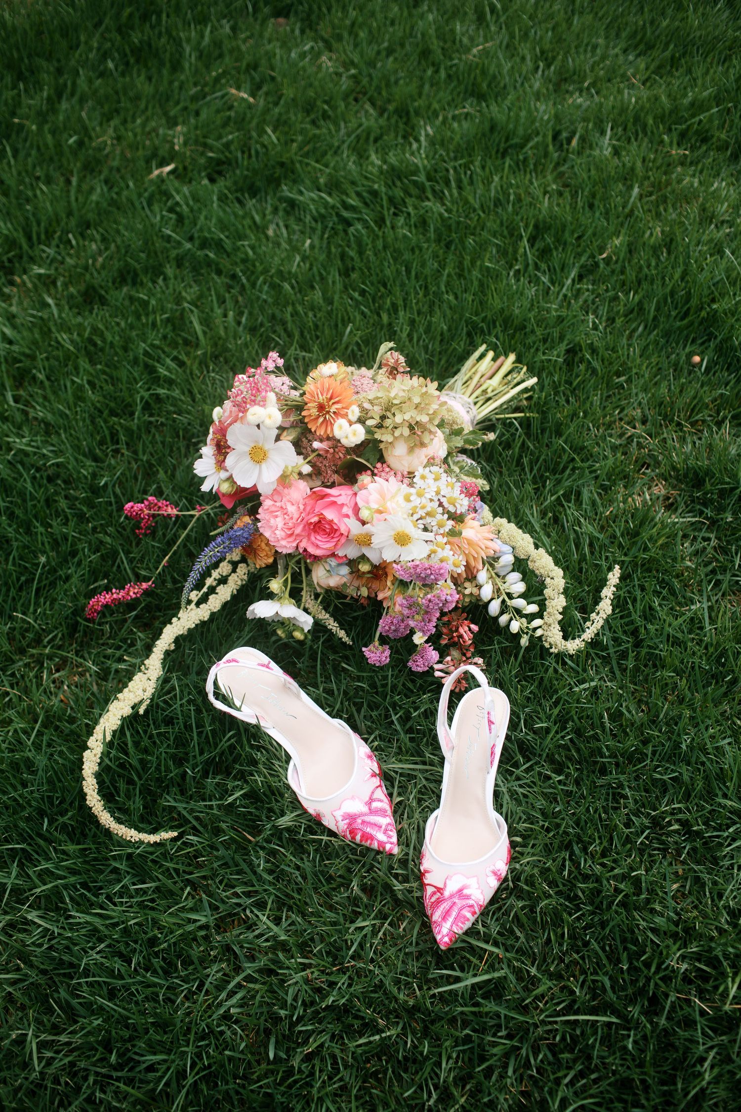 Bridal bouquet in pink, orange, and purple lying next to wedding heels - Adrianna Elizabeth Photography.