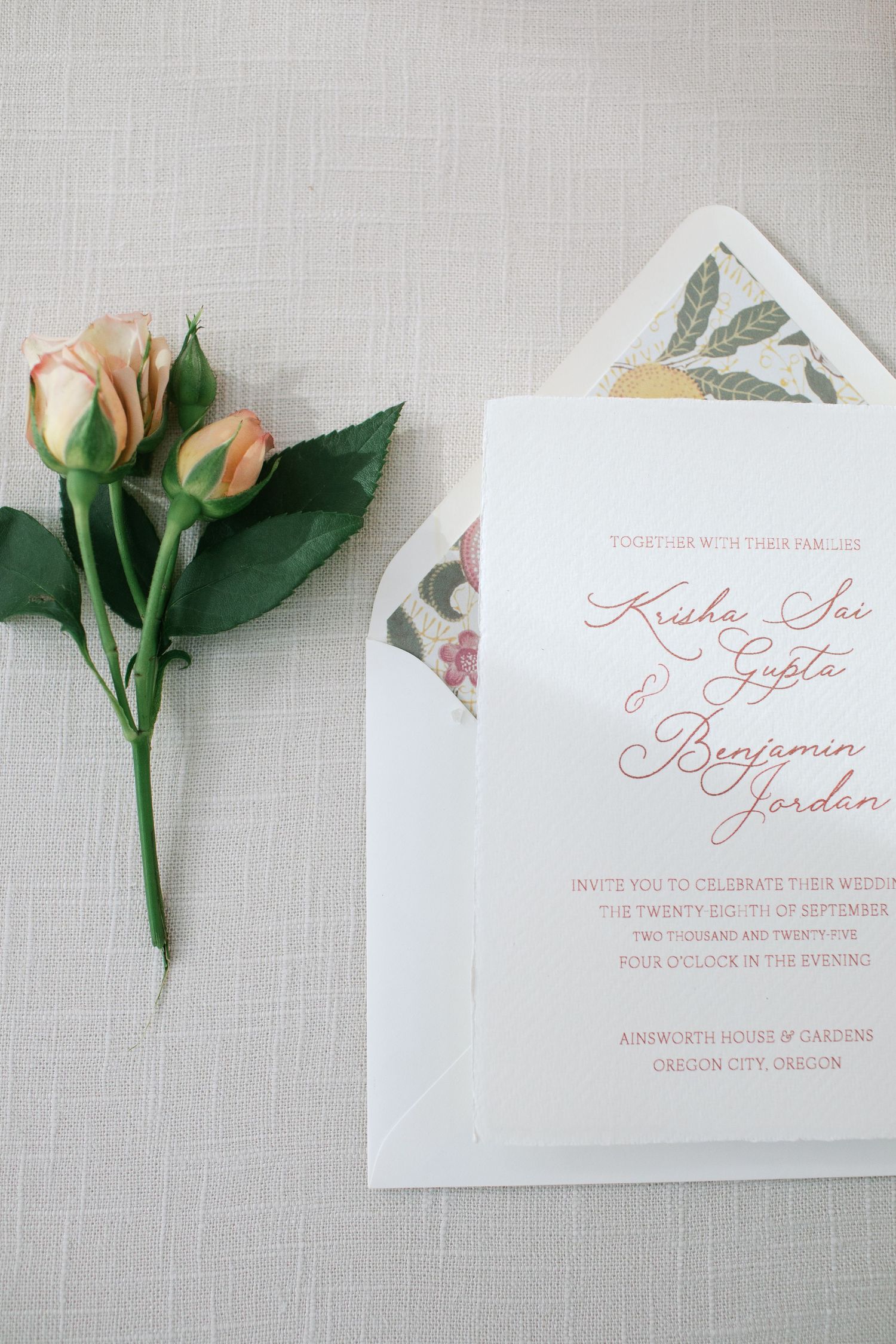 Elegant wedding invitation with calligraphy text and floral design alongside peach roses on a light gray linen background.