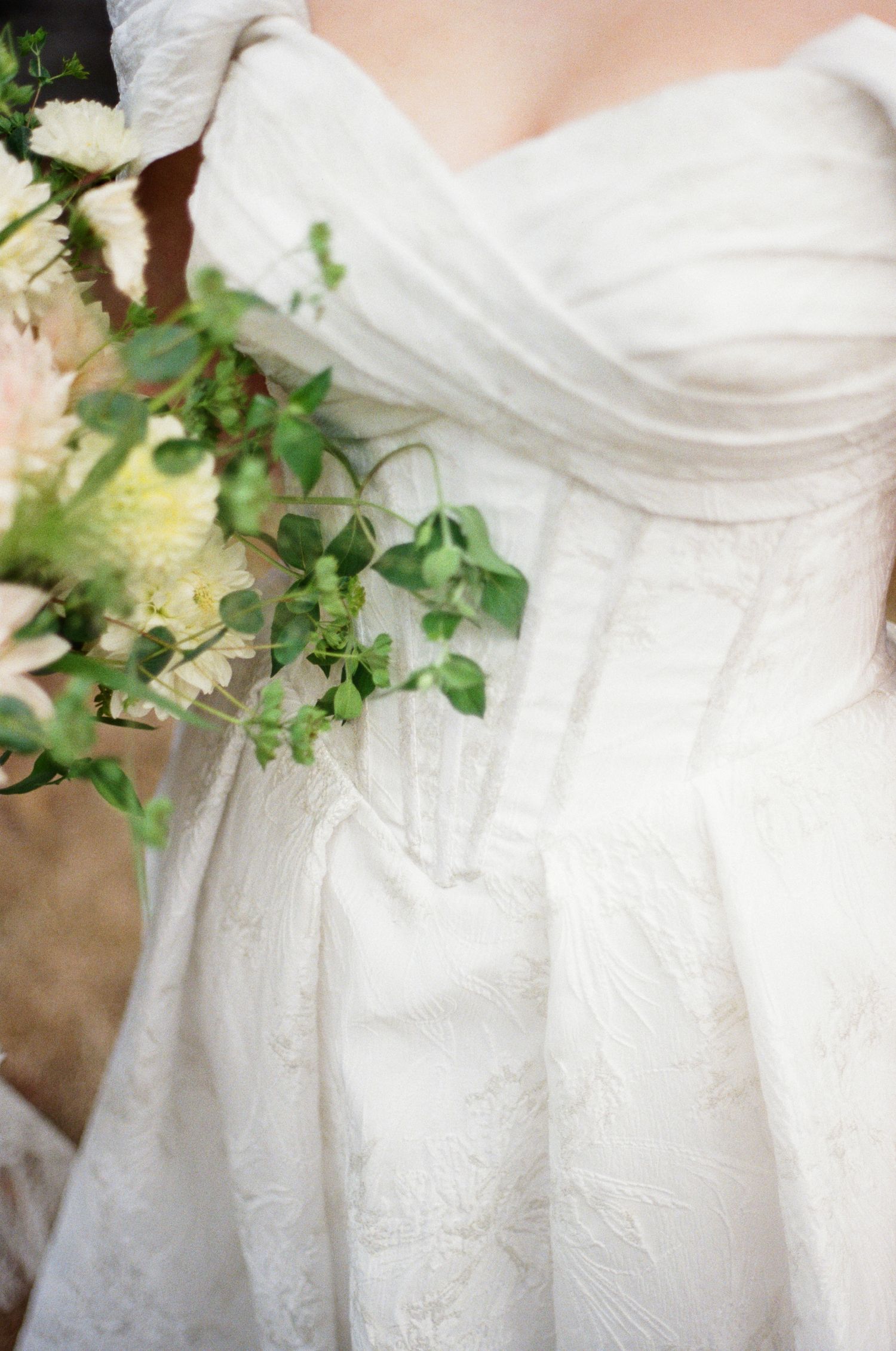 Close-up details of a white lace wedding dress with delicate floral embellishments and green foliage accents.