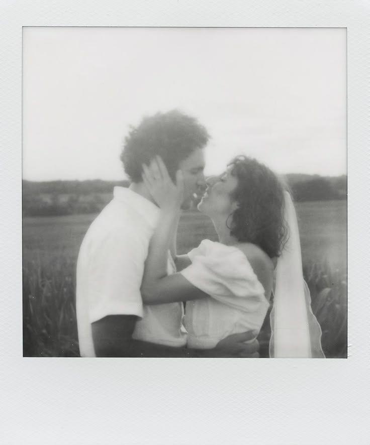 A romantic black and white polaroid photo shows a couple sharing an intimate moment in a field.