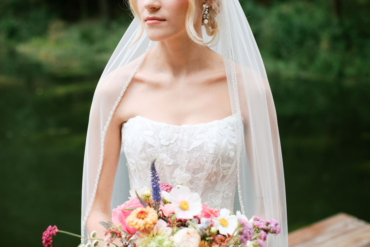 A bridal bouquet featuring vibrant pink, peach and purple flowers with cascading greenery against a white gown.