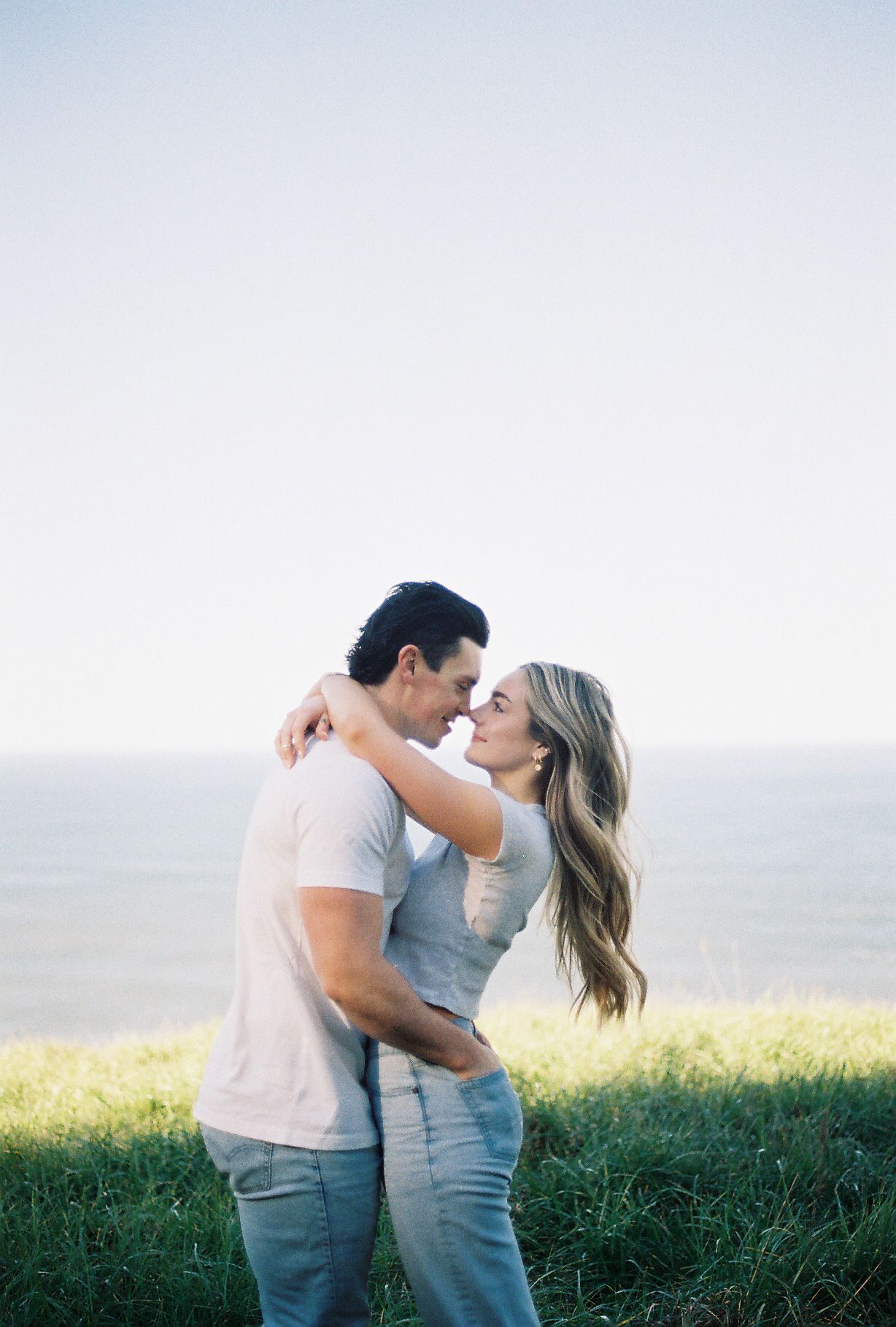 A couple shares romantic moments in a grassy field during sunset, captured in a series of intimate poses.