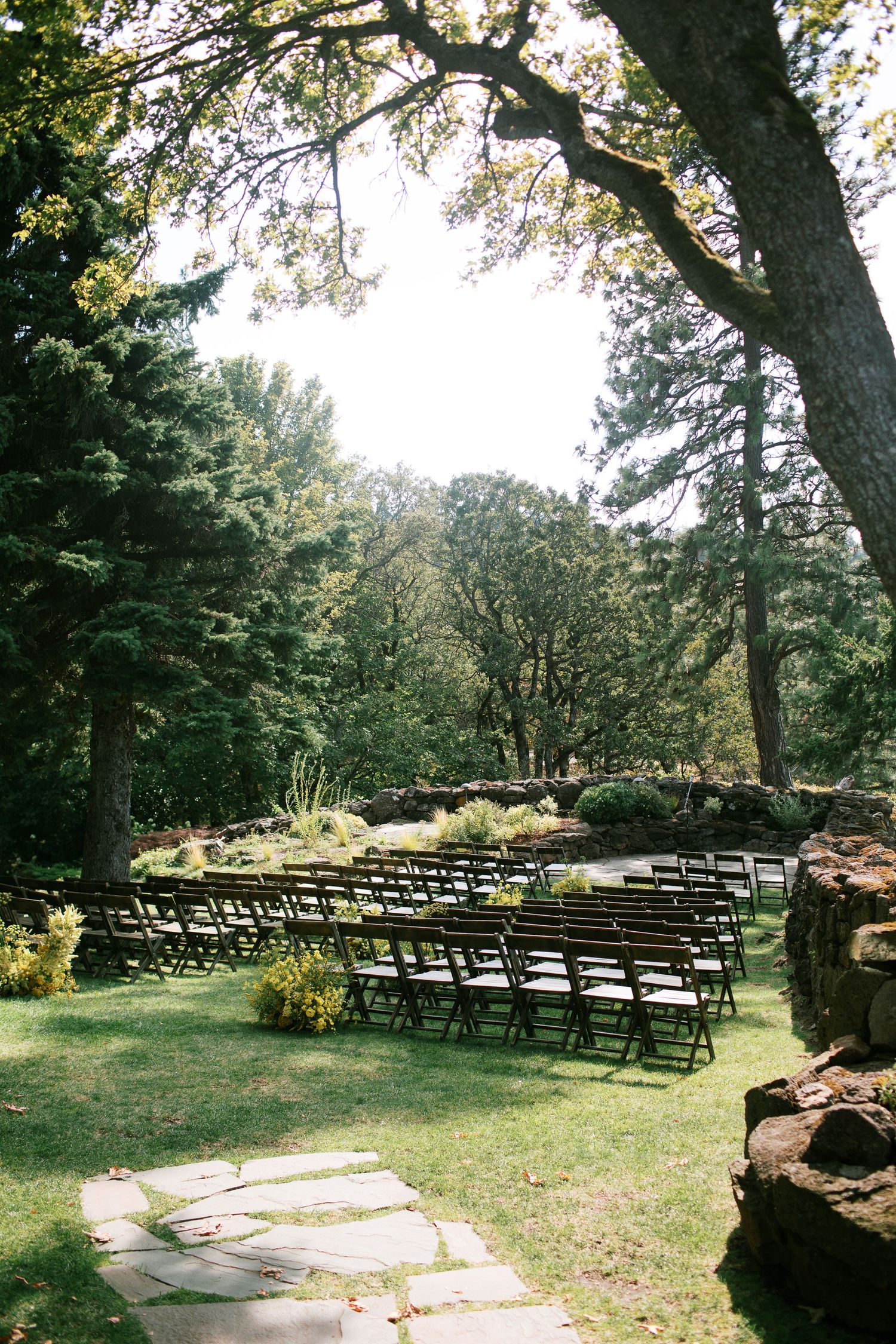 Rows of black folding chairs arranged on a grassy lawn for an outdoor wedding ceremony with trees in the background.