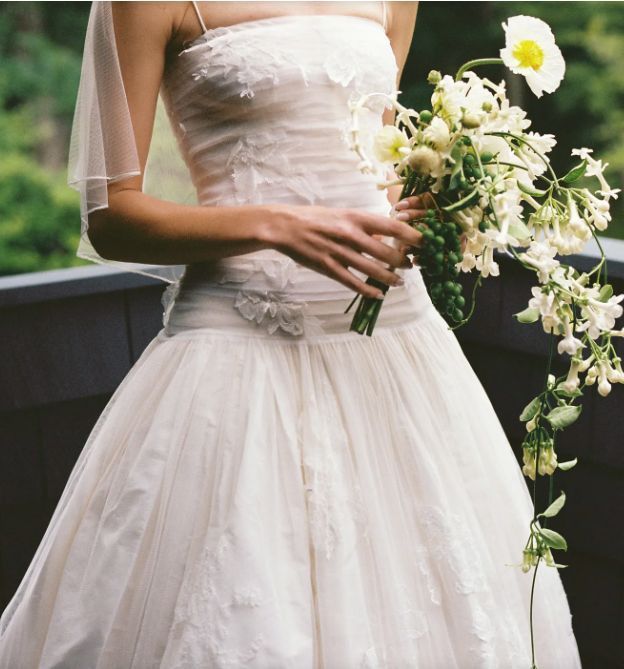 A classic white wedding dress with a strapless bodice and tulle skirt, holding a bouquet of white lilies and daisies.