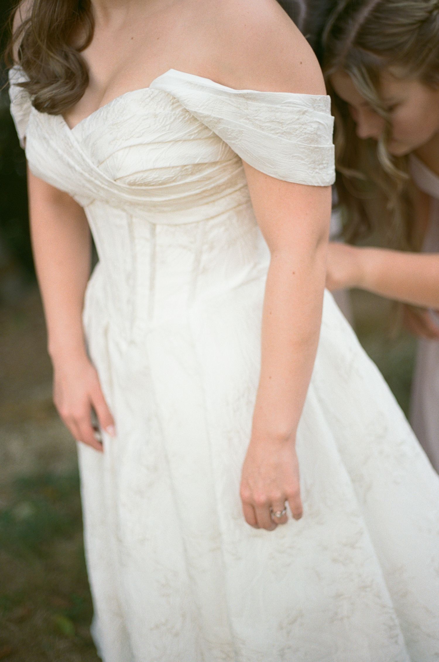 Close-up details of white wedding dresses showing off-shoulder necklines and gathered fabric textures on 35mm film.