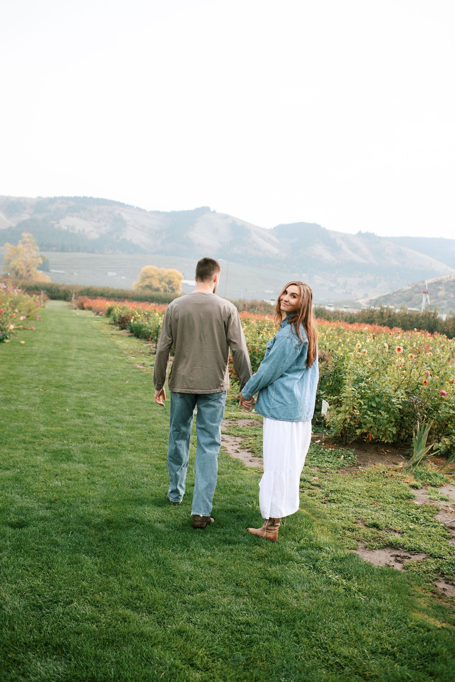 A couple walks together through a scenic mountain meadow on a sunny autumn afternoon.