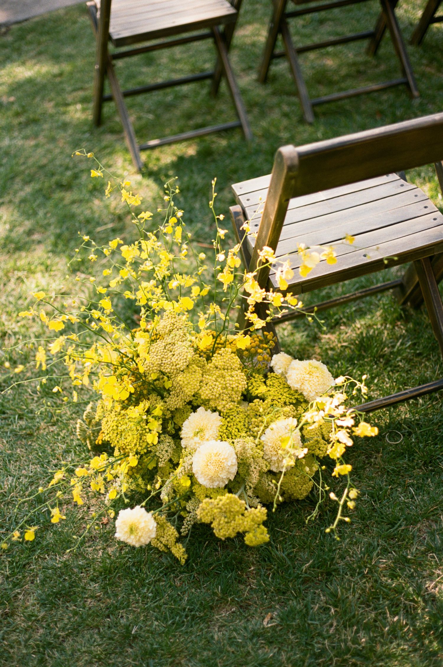 Yellow and white floral arrangements with delicate blooms rest on lush green grass beside wooden benches.