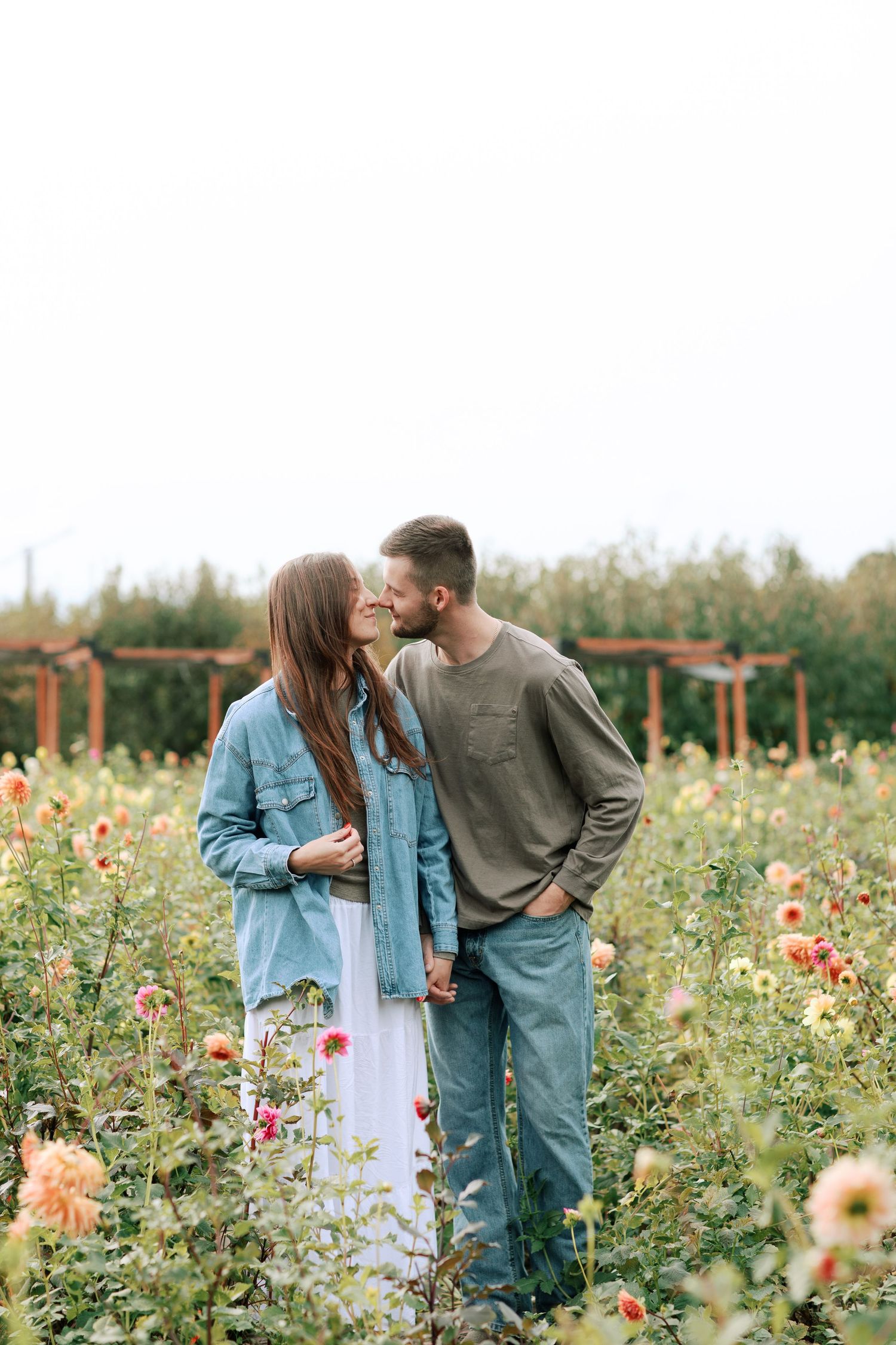 Couple sharing romantic moments in a vibrant flower field with wildflowers and dahlias on a sunny day.