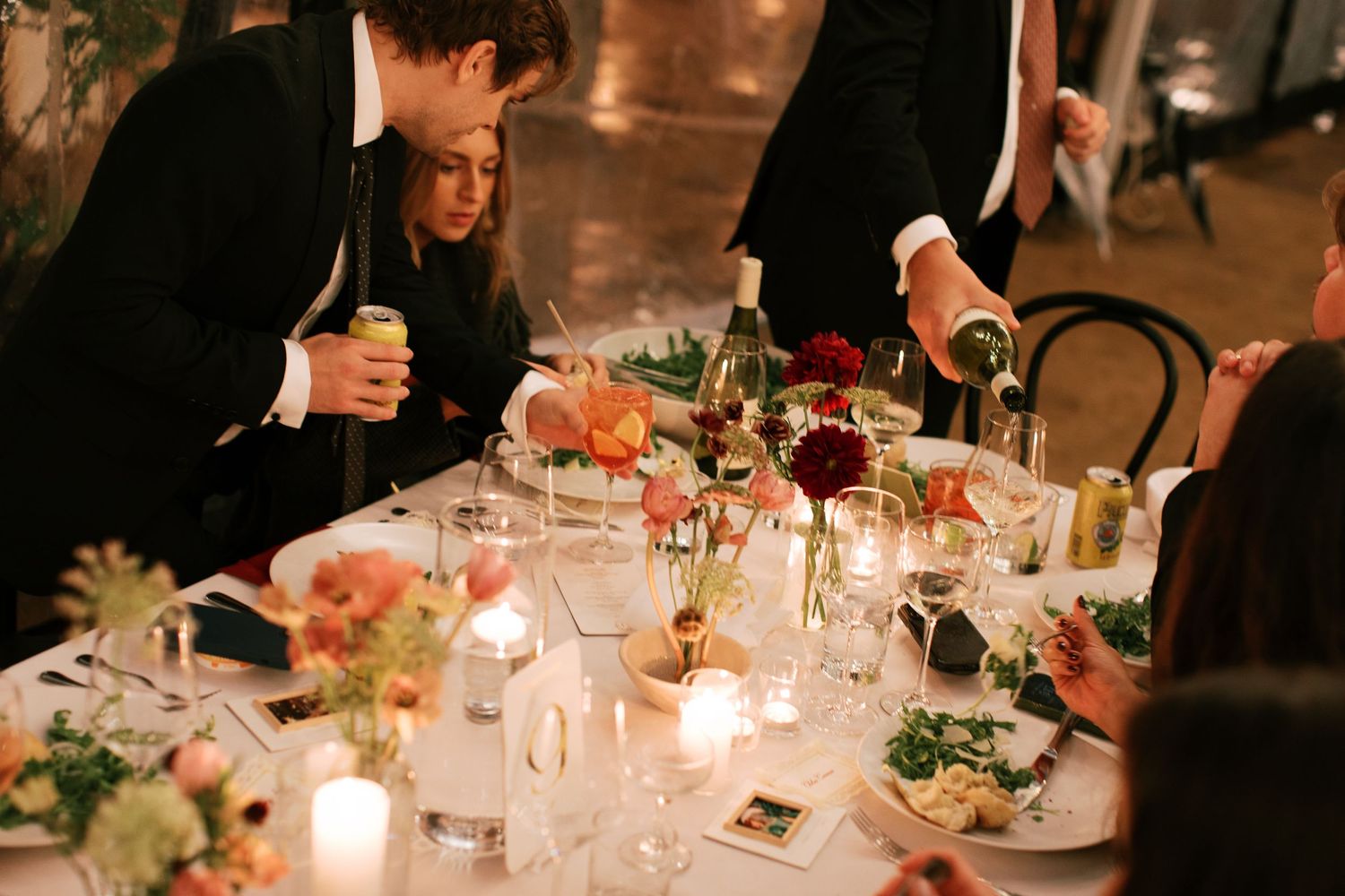 Elegant candlelit wedding reception tables decorated with floral centerpieces and glowing votives create a romantic atmosphere.
