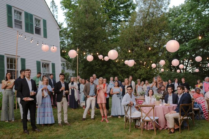 Wedding guests gather outdoors at dusk under glowing paper lanterns at a backyard garden reception.